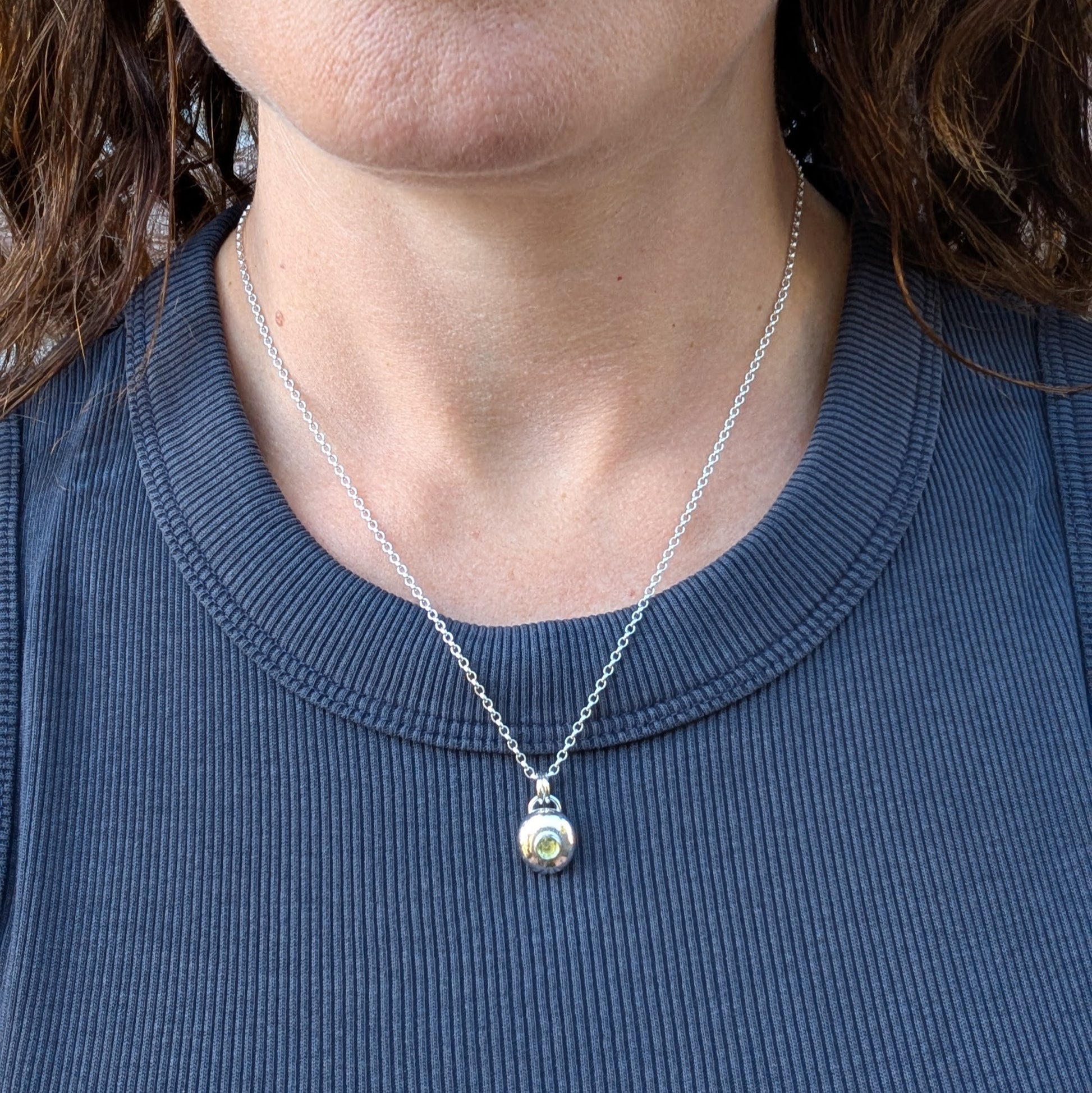 Silver pebble necklace with Peridot worn on a chain, shown against a dark top.