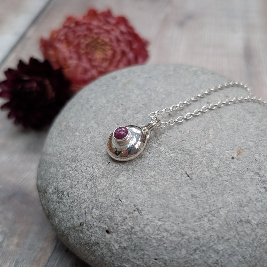 Close-up of a silver pebble necklace with ruby pendant, showing the raised ruby stone set in a polished silver pebble.
