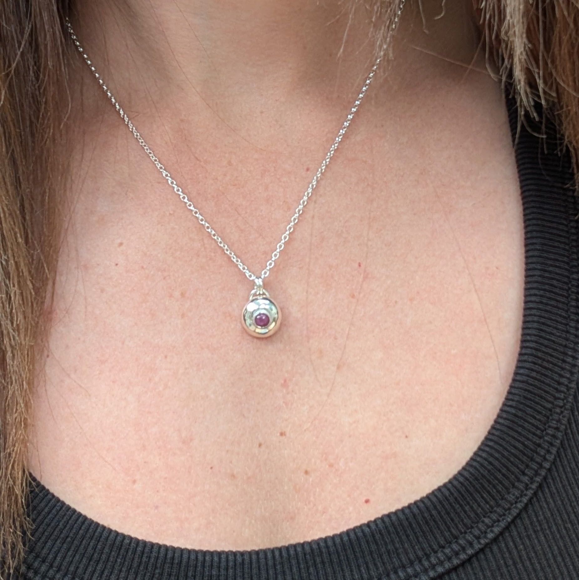 Silver pebble necklace with ruby pendant being worn, showing its delicate size and simple silver chain.