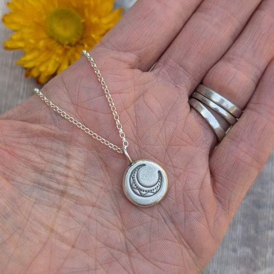 Silver Pebble Stamped Moon Necklace resting in a hand, showing the crescent moon design on a round silver pendant.