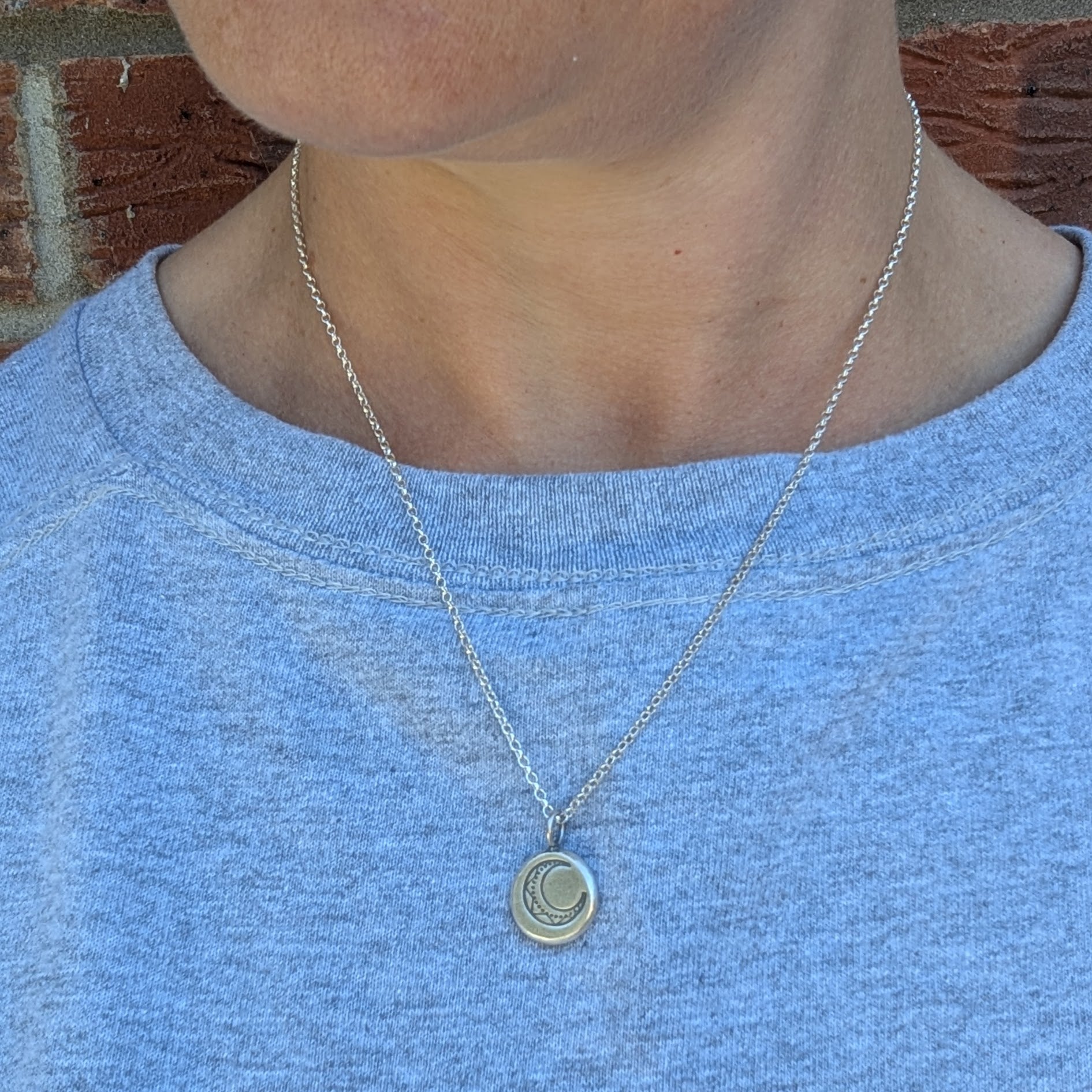 Silver Pebble Stamped Moon Necklace being worn on a silver chain against a grey top.