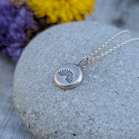Silver pebble stamped sunburst necklace displayed on a smooth stone.