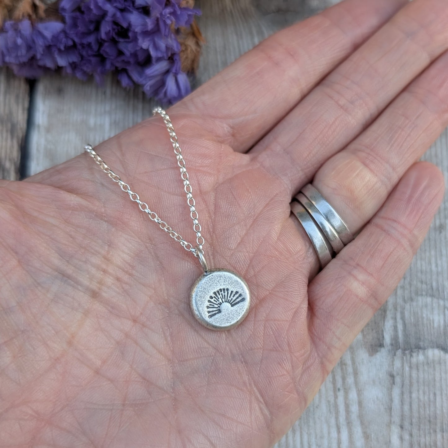 Hand holding silver pebble stamped sunburst necklace, showing the small pendant detail.