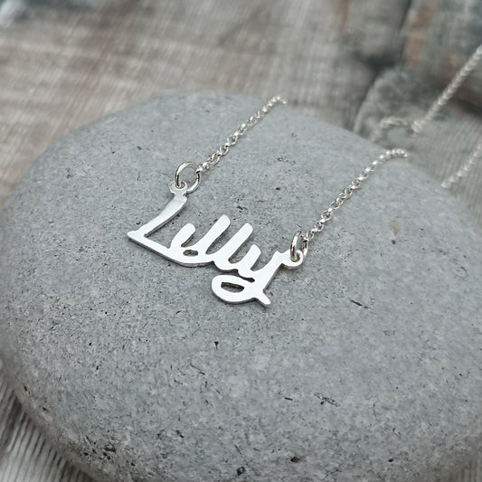 silver personalised name necklace shown displayed on a grey stone. 
