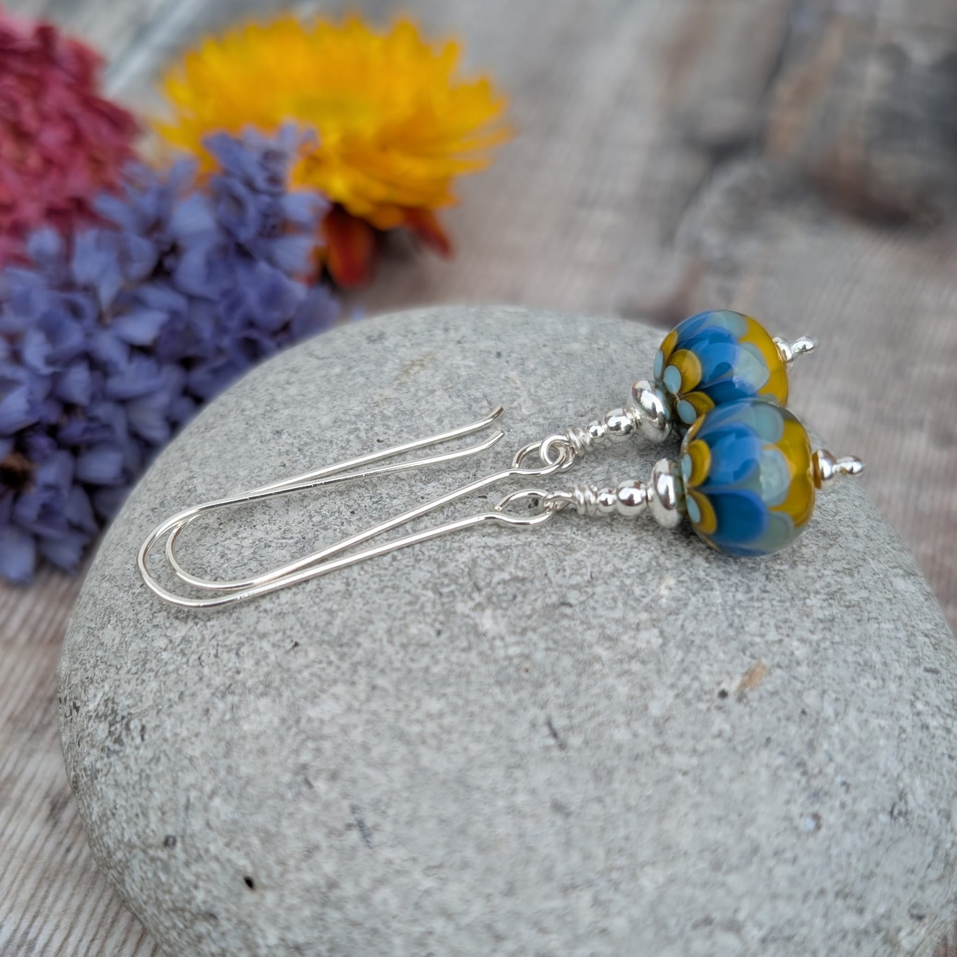 Close-up of Silver petals lampwork glass bead earrings highlighting the layered petal pattern in blue, pale aqua, and mustard yellow within the handmade glass beads.