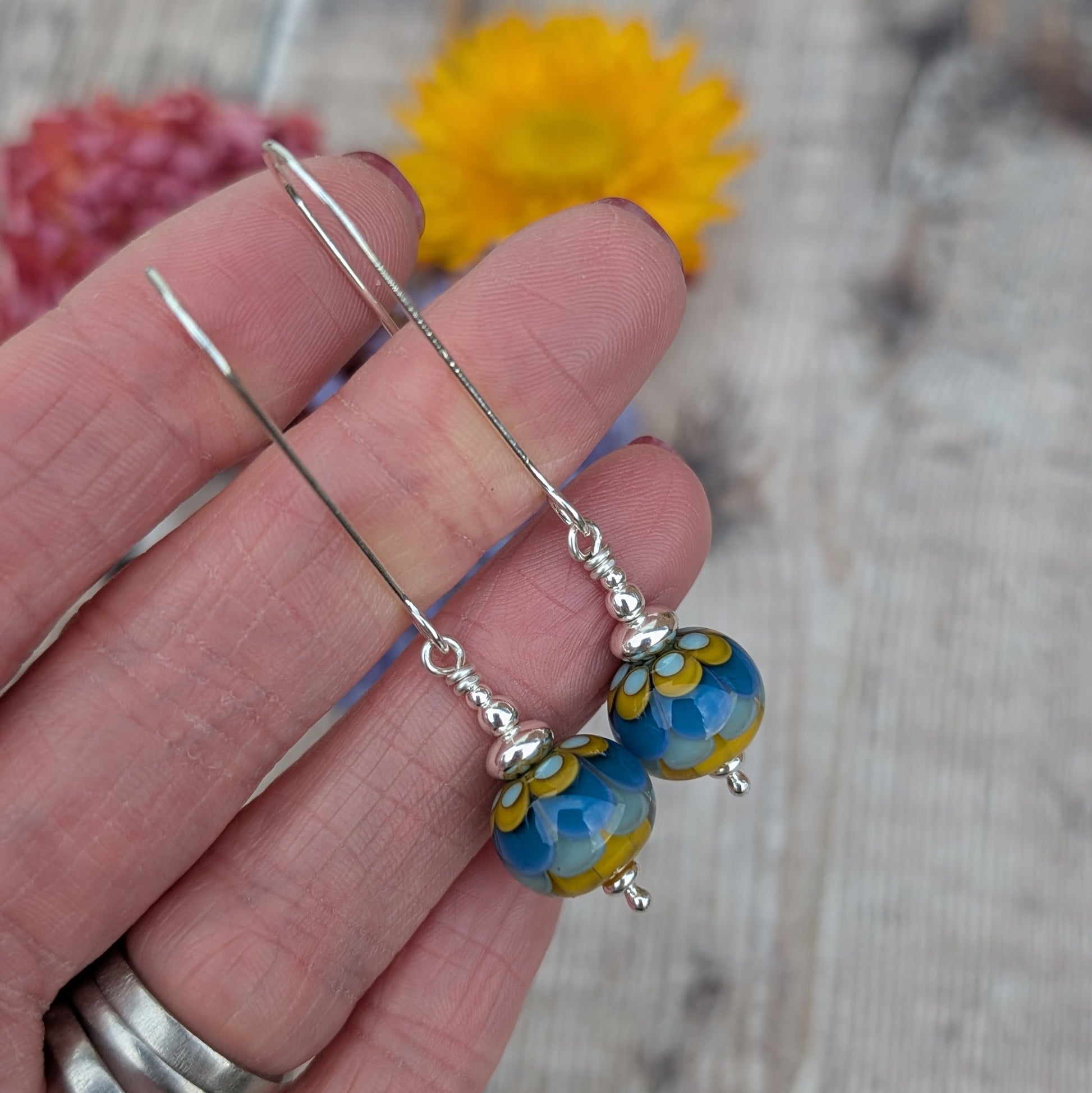 Silver petals lampwork glass bead earrings held between fingers, showing the scale of the round lampwork glass beads and the silver wire and bead details.