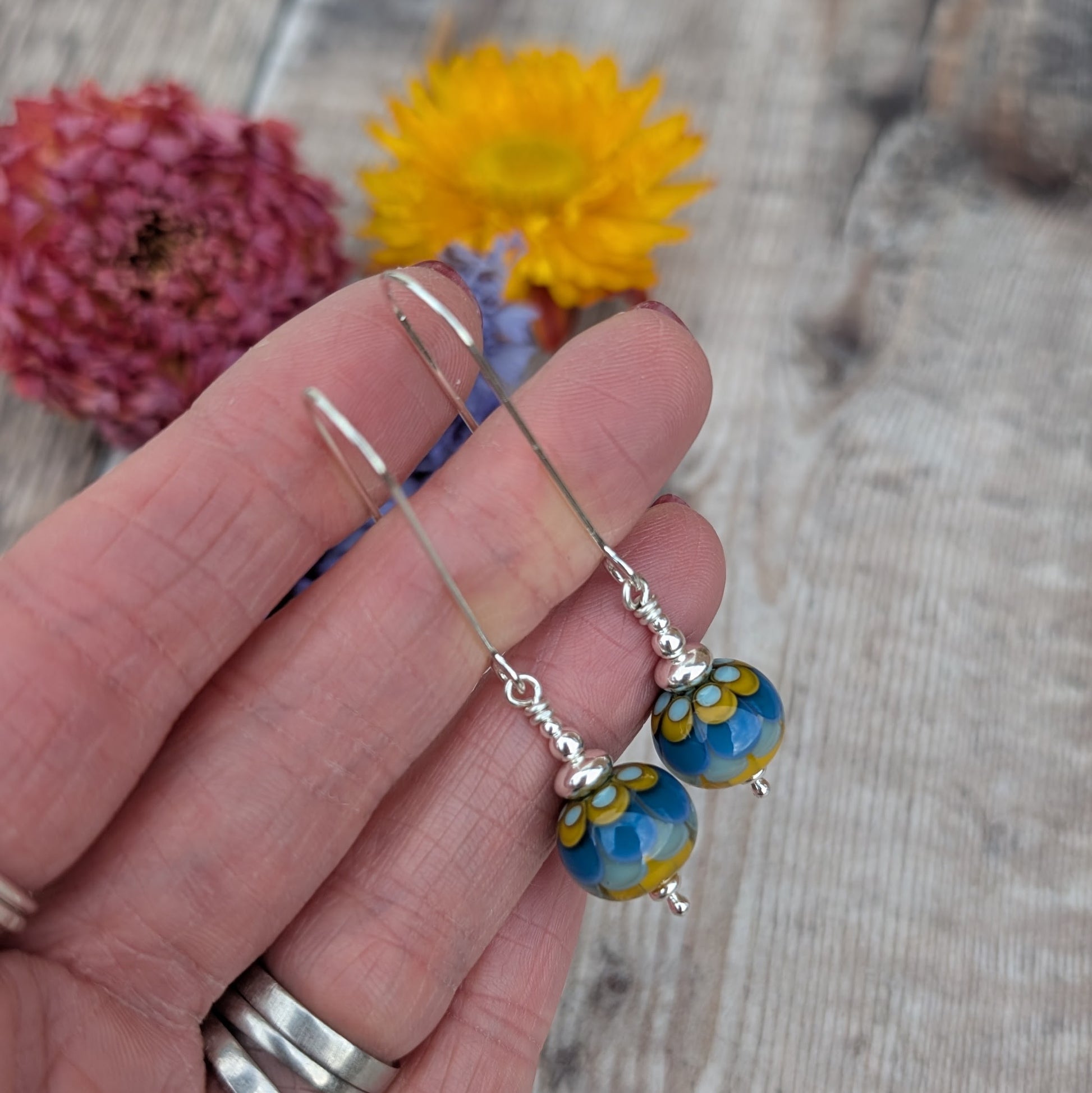 Silver petals lampwork glass bead earrings shown from a slightly different angle in hand, focusing on the handmade glass bead pattern and silver findings.