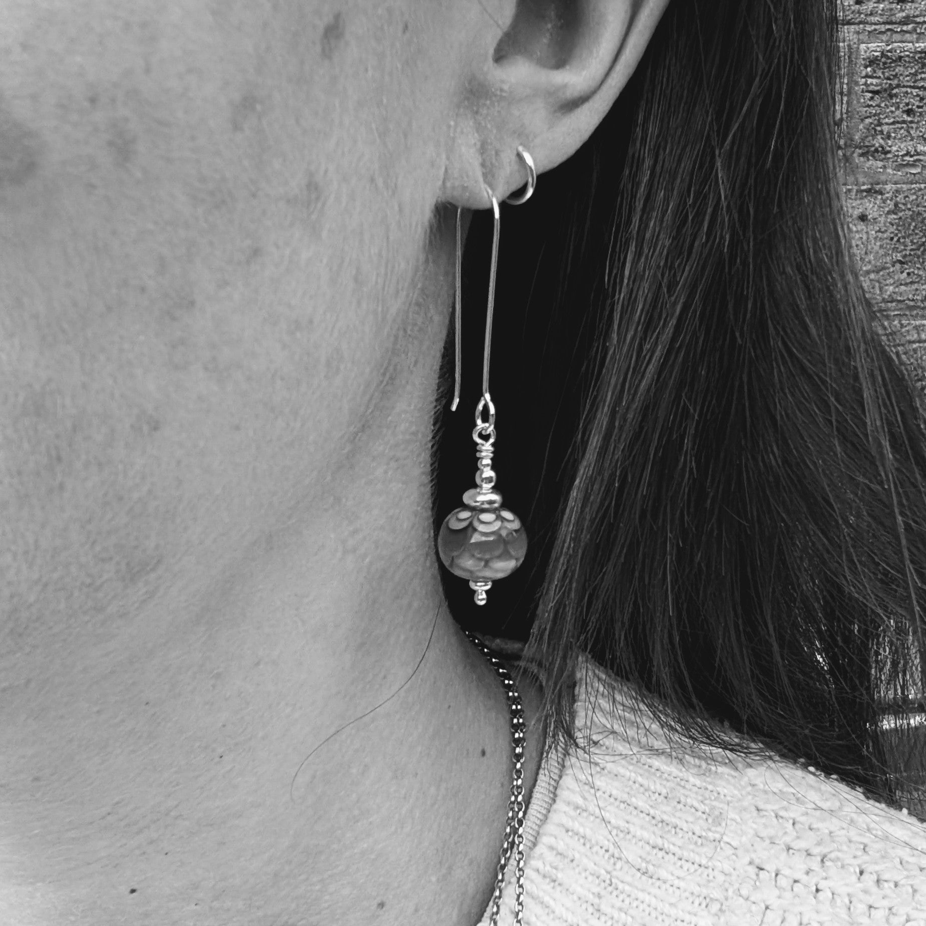 Silver petals lampwork glass bead earrings worn in the ear, showing the length of the silver ear wires and how the glass bead drops sit when worn.
