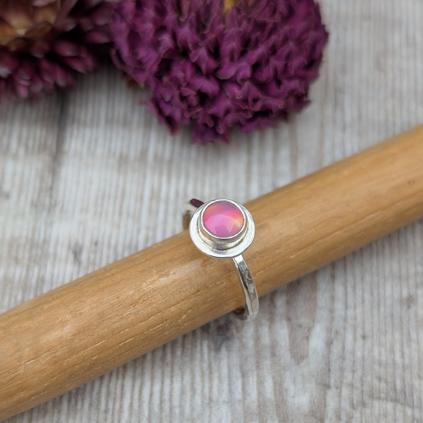 Handmade sterling silver pink aurora opal ring shown on a wooden ring mandrel, highlighting the polished finish and round stone setting.