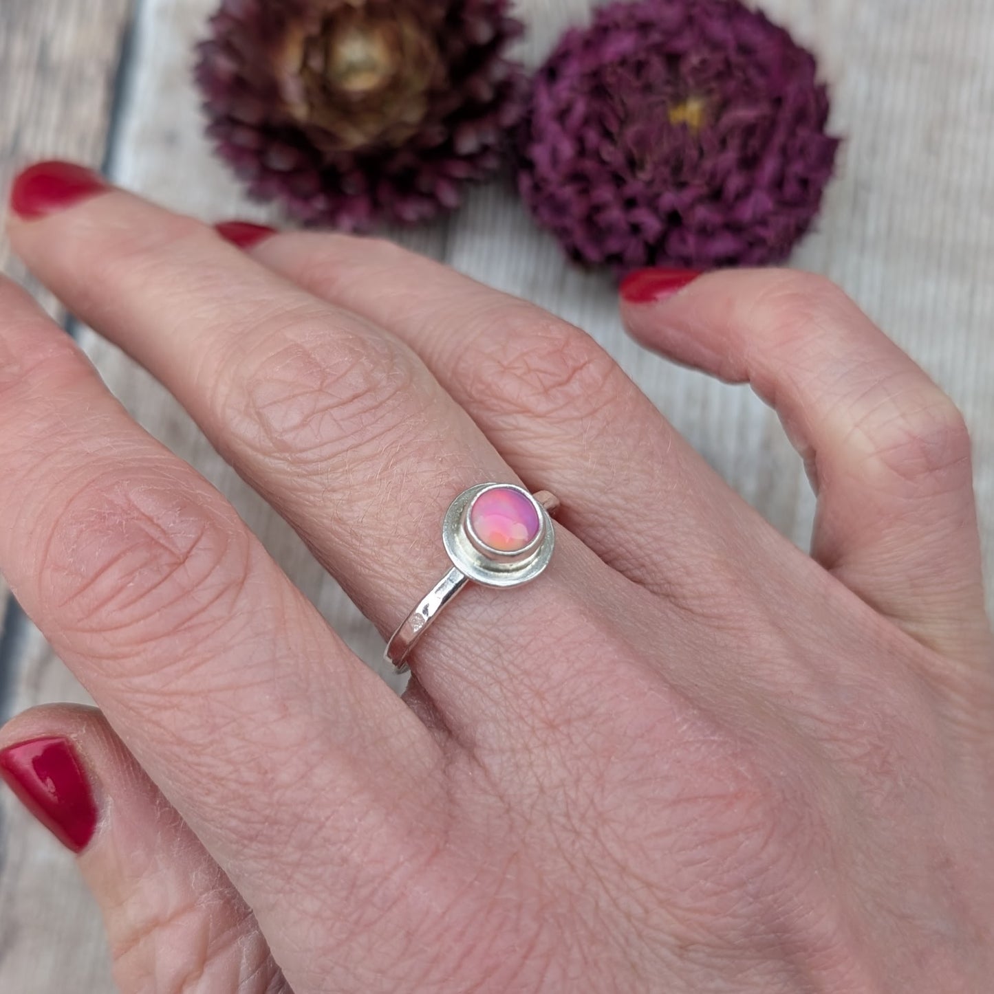 Sterling silver stacking ring with a pink aurora opal worn on the finger, showing the slim band and soft colour of the stone.