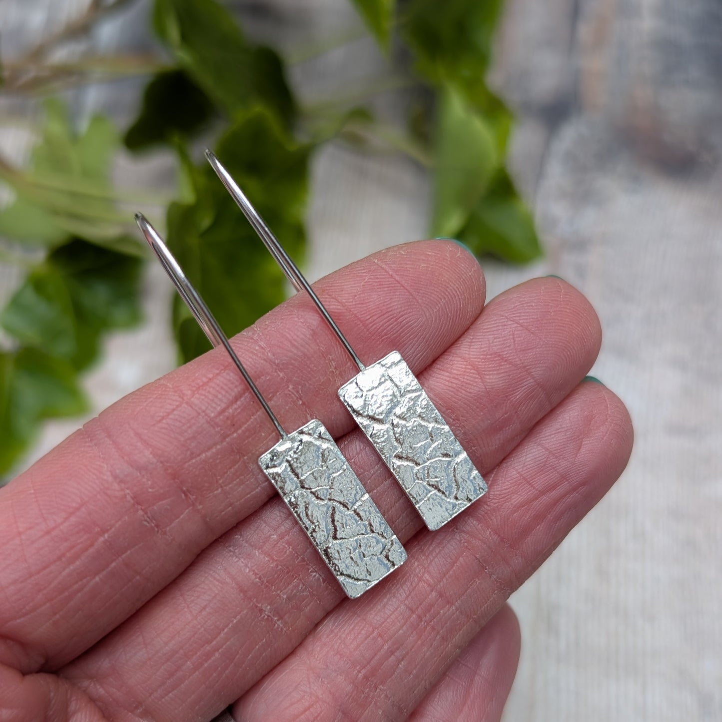 Close-up of Silver Rectangle Earrings with Cracked Earth Pattern held in hand highlighting pressed pattern detail
