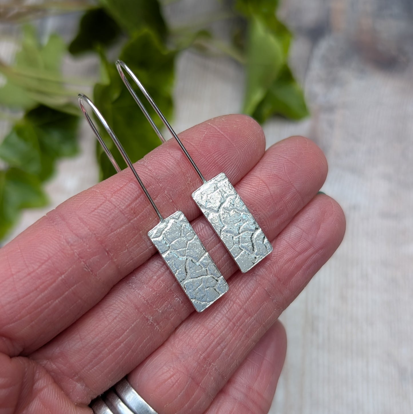 Silver Rectangle Earrings with Cracked Earth Pattern held in hand showing front detail of textured surface