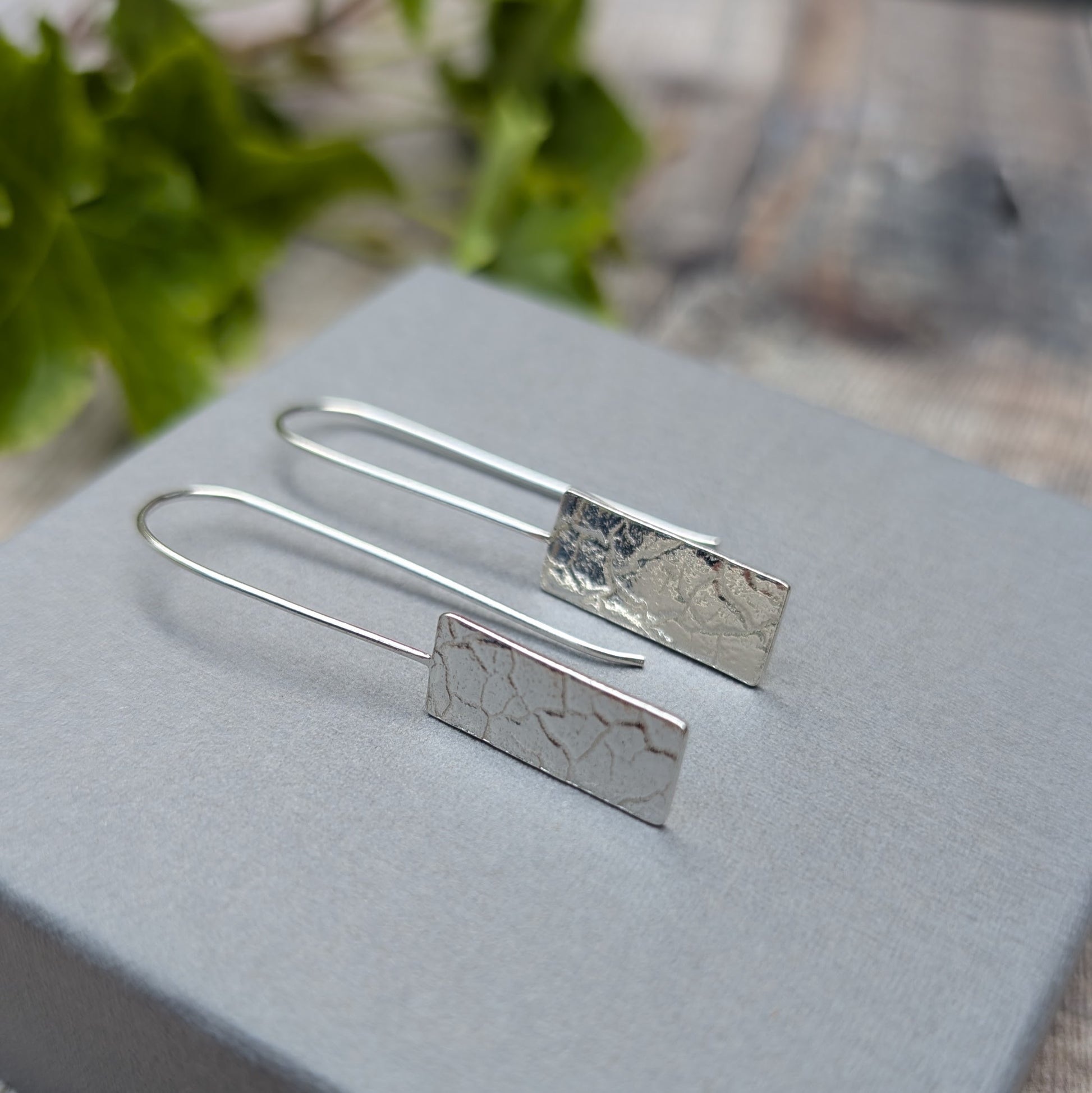 Silver Rectangle Earrings with Cracked Earth Pattern resting on grey box with textured surface visible