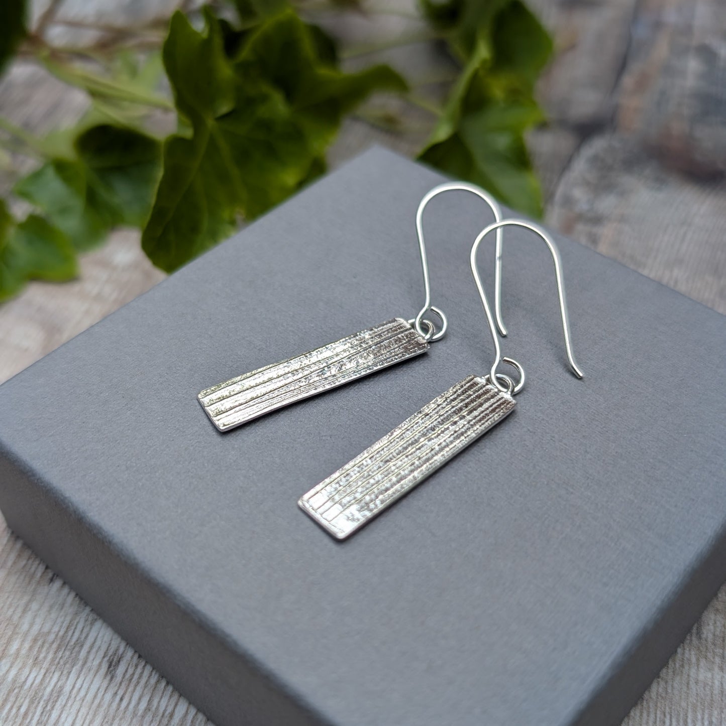 Silver Rectangle Earrings with Ribbon Pattern displayed on a grey box with soft natural background
