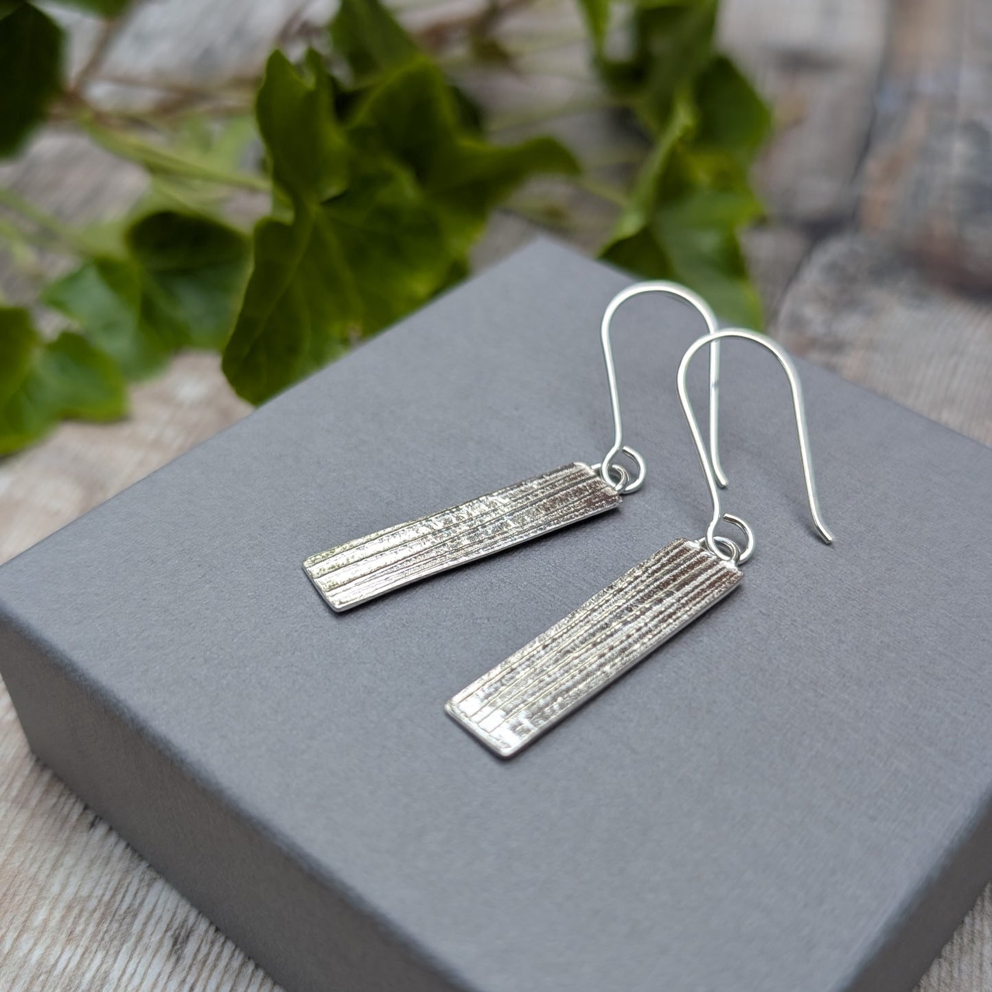 Silver Rectangle Earrings with Ribbon Pattern shown at an angle on a grey display box
