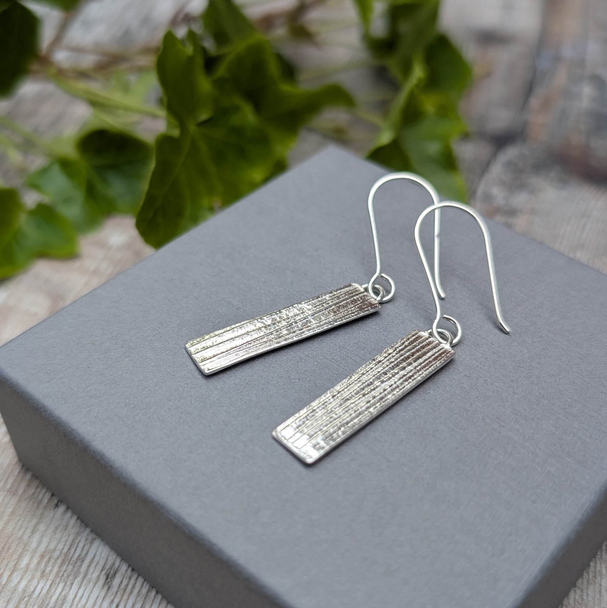 Silver Rectangle Earrings with Ribbon Pattern shown at an angle on a grey display box