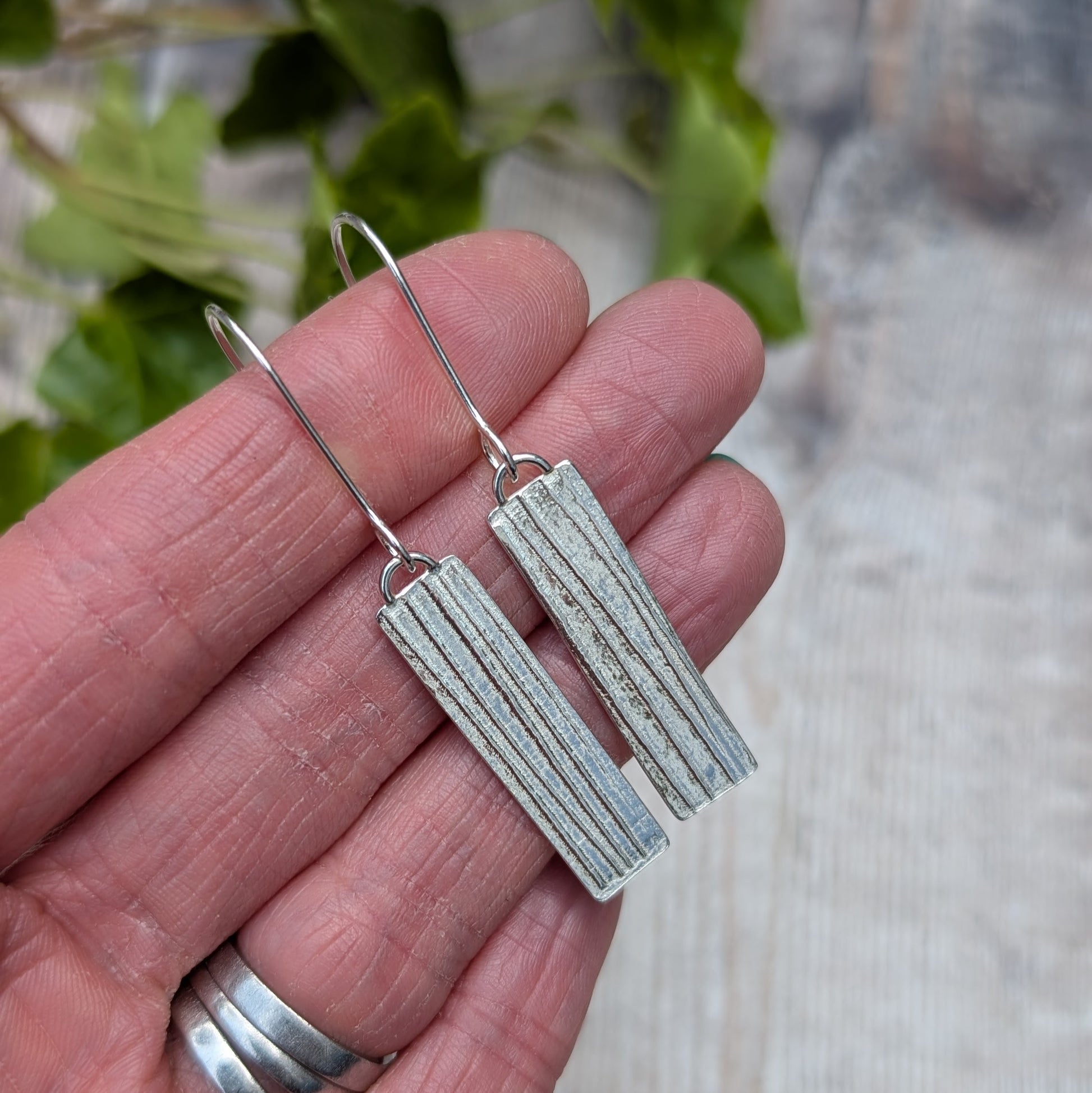 Close-up of Silver Rectangle Earrings with Ribbon Pattern in hand highlighting the pressed pattern