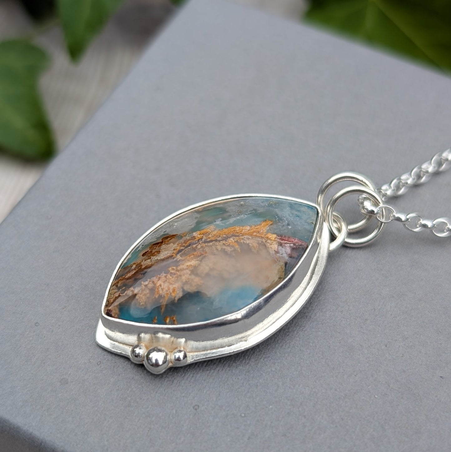 Detailed side view of a Silver Regency Rose Plume Agate Necklace with a handmade recycled Sterling Silver setting and decorative silver bead details.
