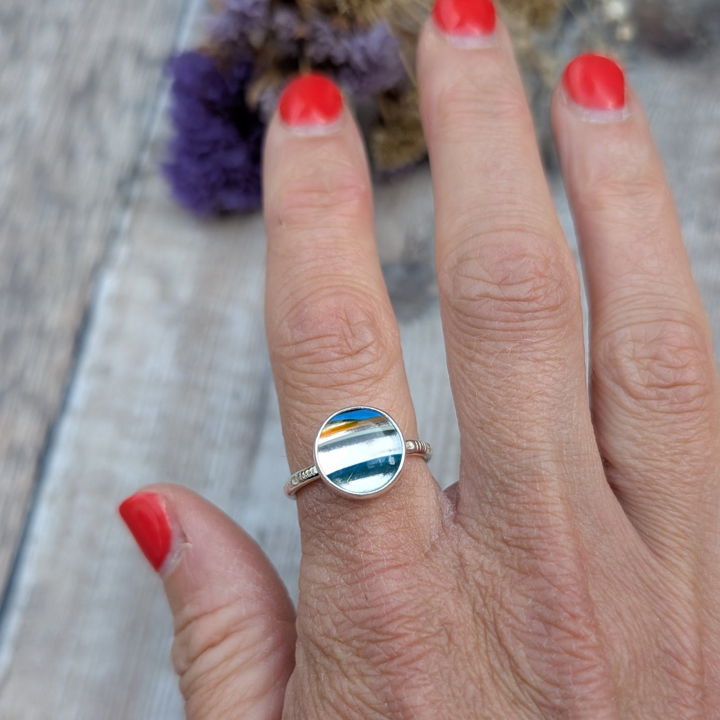 Close-up of a colourful round Surfite ring worn on a hand, showing the striped layers of blue, white and amber.
