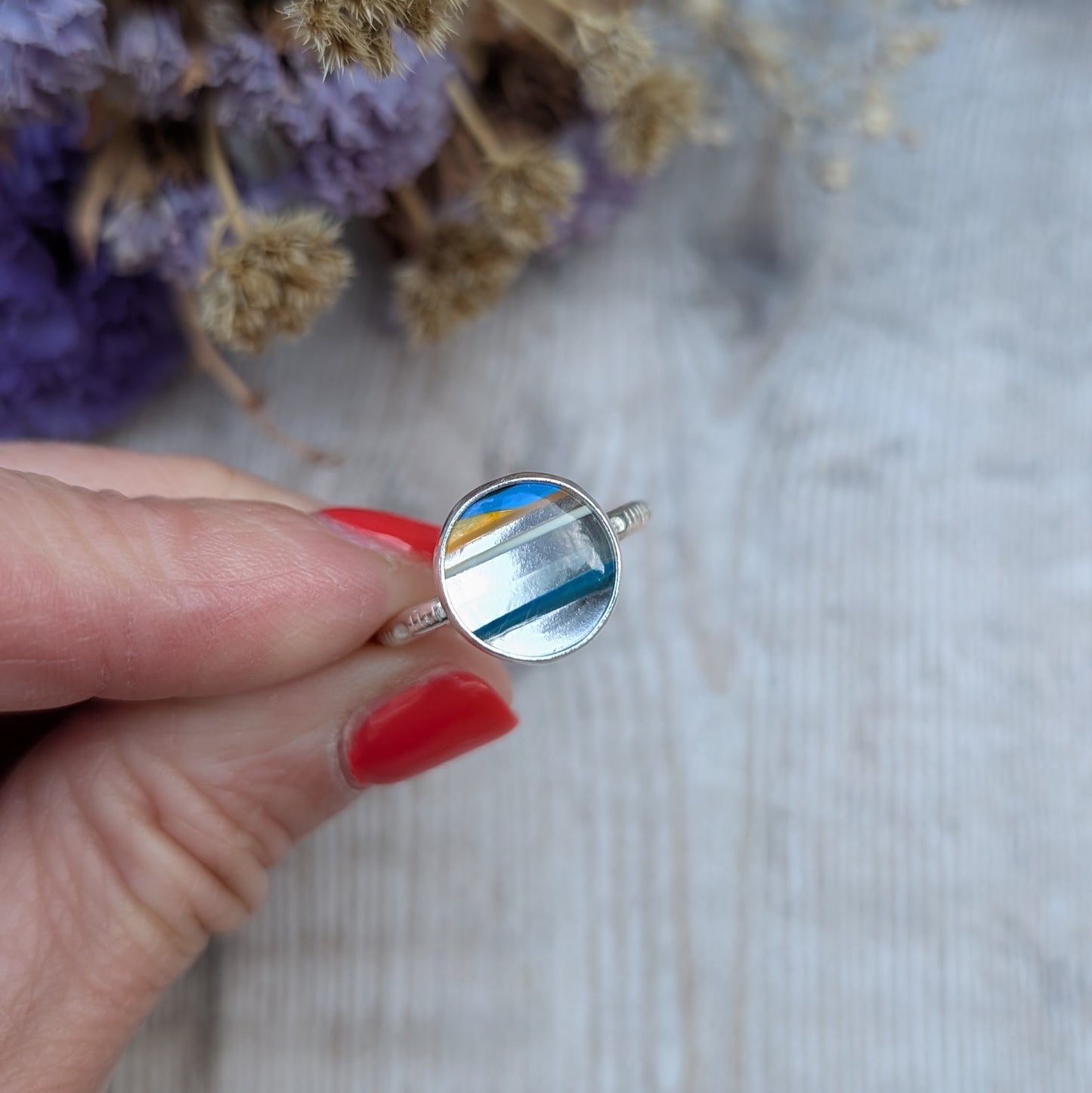 Handmade Surfite ring held between fingers, highlighting the recycled sterling silver band and round stone setting.