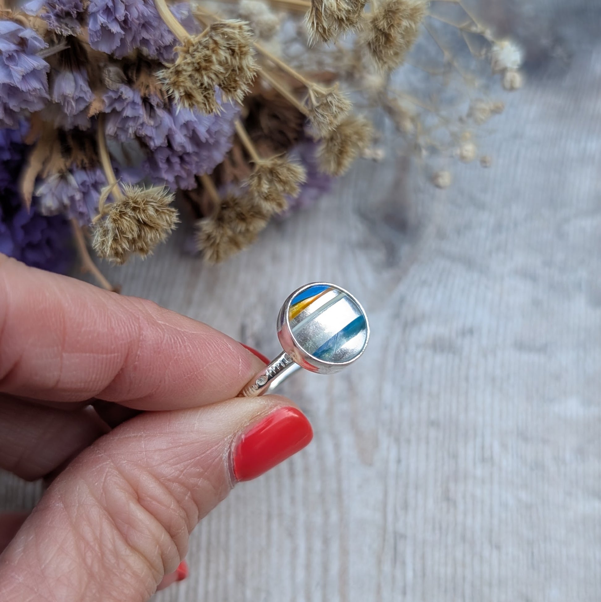 Handmade Surfite ring held between fingers, highlighting the recycled sterling silver band and round stone setting.
