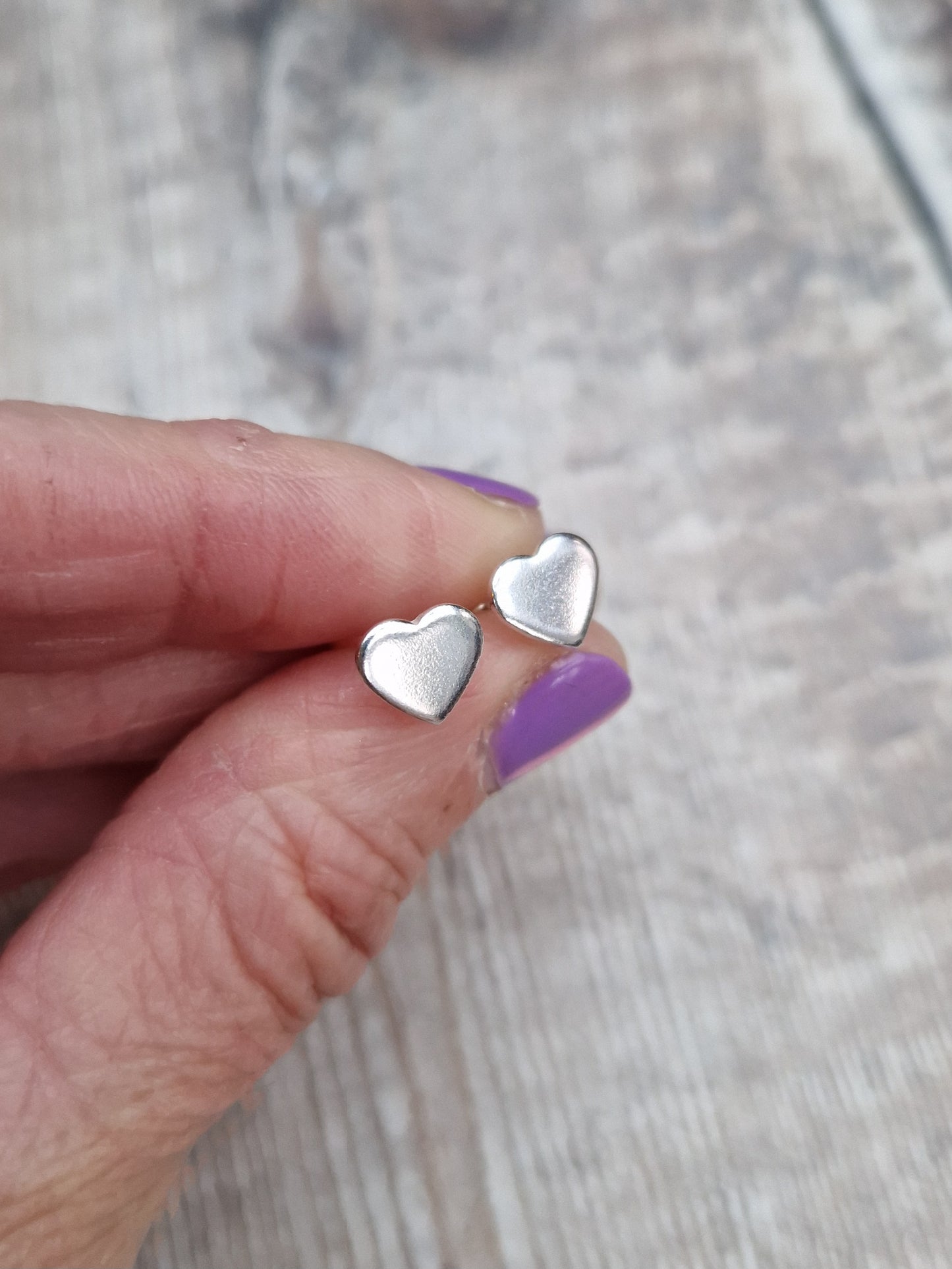 Each earring is a small silver heart shape, flat and smooth, mounted on a silver stud bar.