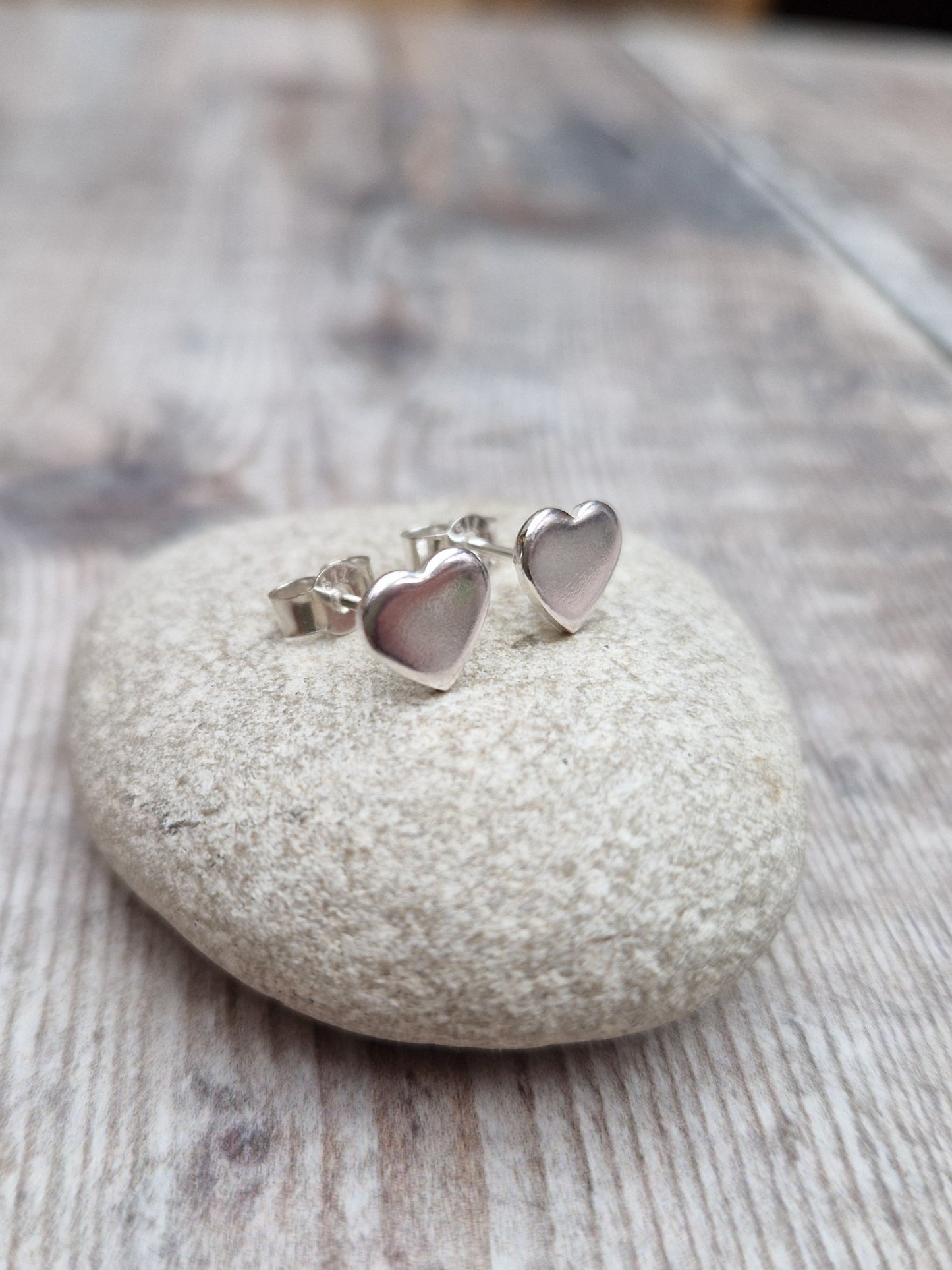 Each earring is a small silver heart shape, flat and smooth, mounted on a silver stud bar.