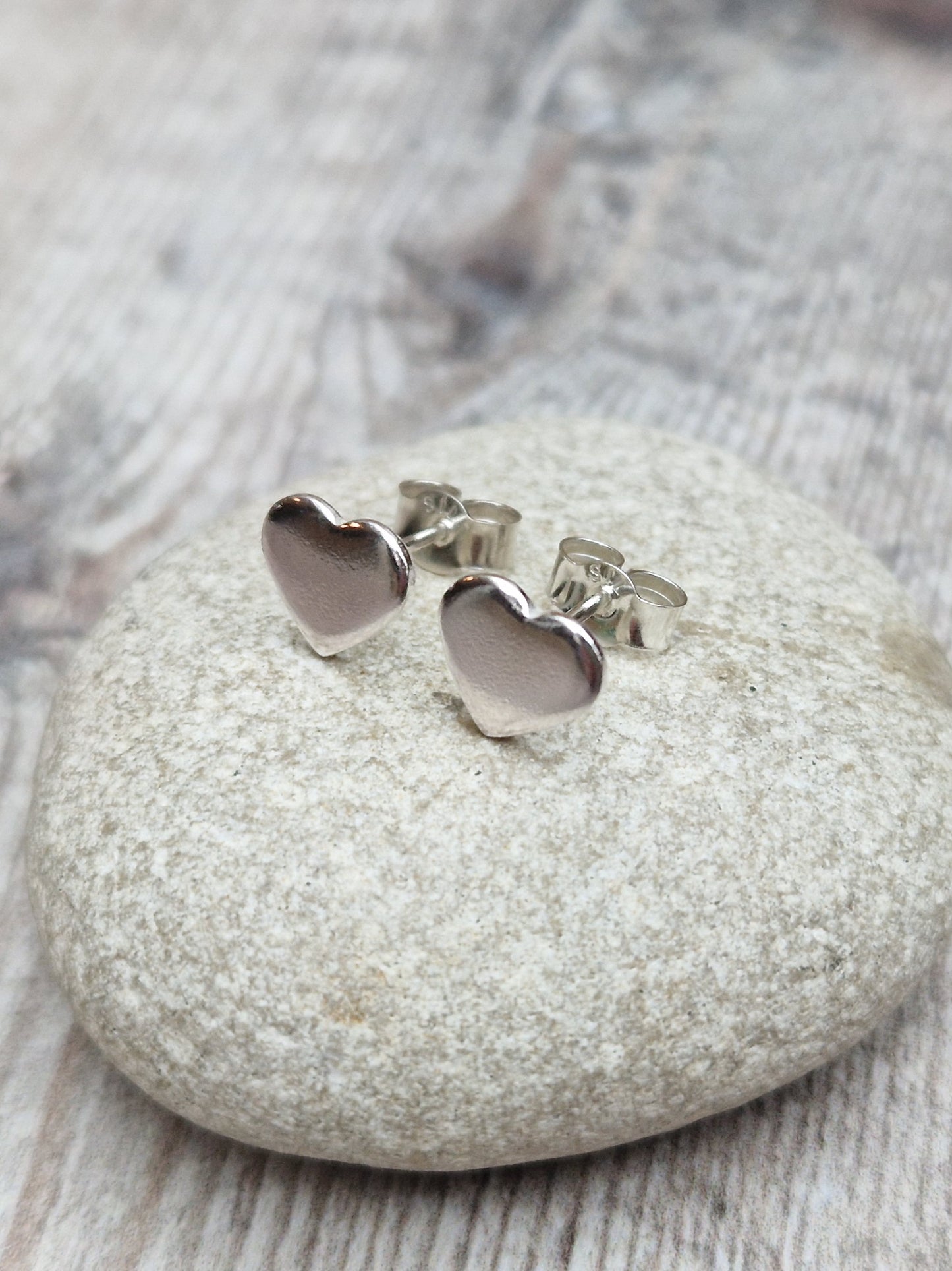 Each earring is a small silver heart shape, flat and smooth, mounted on a silver stud bar.