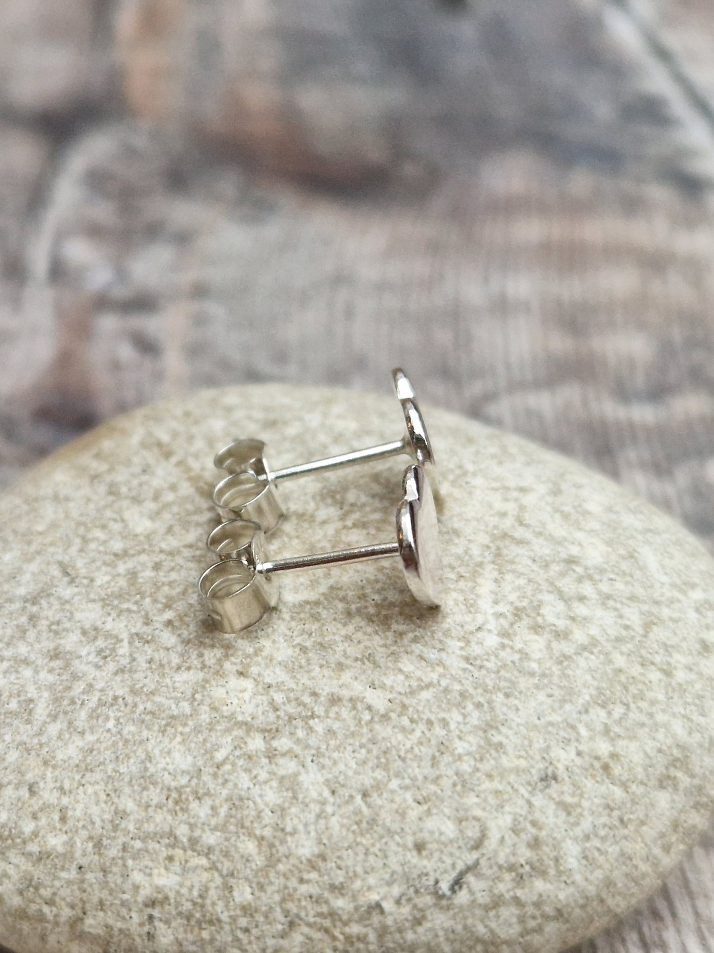 Each earring is a small silver heart shape, flat and smooth, mounted on a silver stud bar.