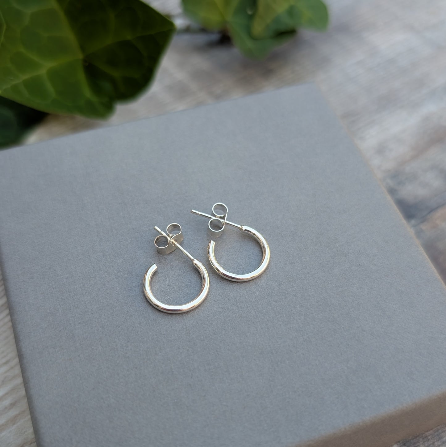Close up of Silver small smooth hoop earrings handmade from recycled Sterling Silver displayed on fingertips.