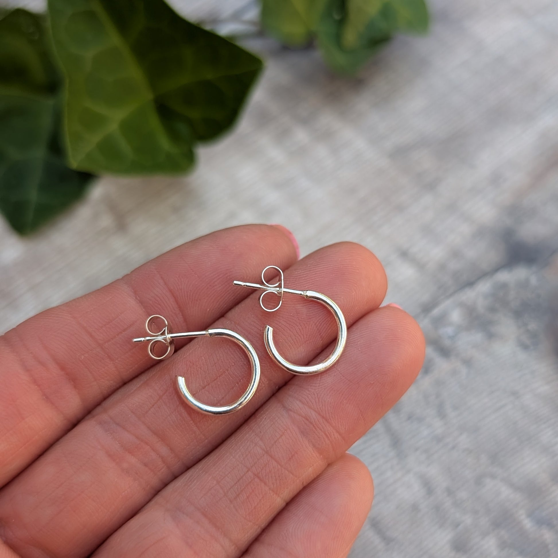 Silver small smooth hoop earrings handmade from recycled Sterling Silver shown resting on fingertips to show their size.