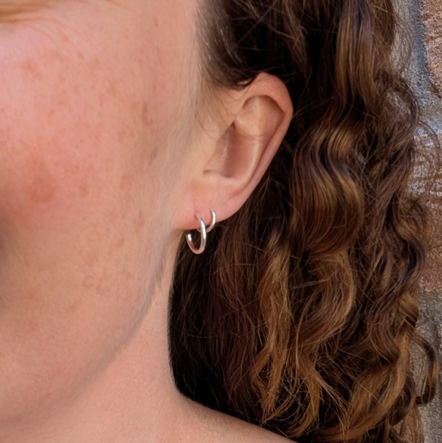Silver small smooth hoop earrings handmade from recycled Sterling Silver being worn in the ear to show their size and fit.