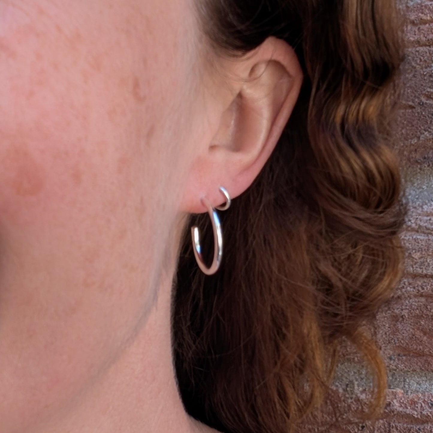 Silver smooth hoop earrings handmade from recycled Sterling Silver being worn in the ear, showing their everyday size and fit.