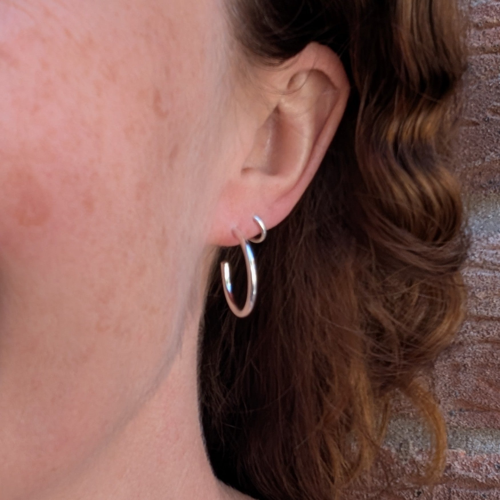 Silver smooth hoop earrings handmade from recycled Sterling Silver being worn in the ear, showing their everyday size and fit.