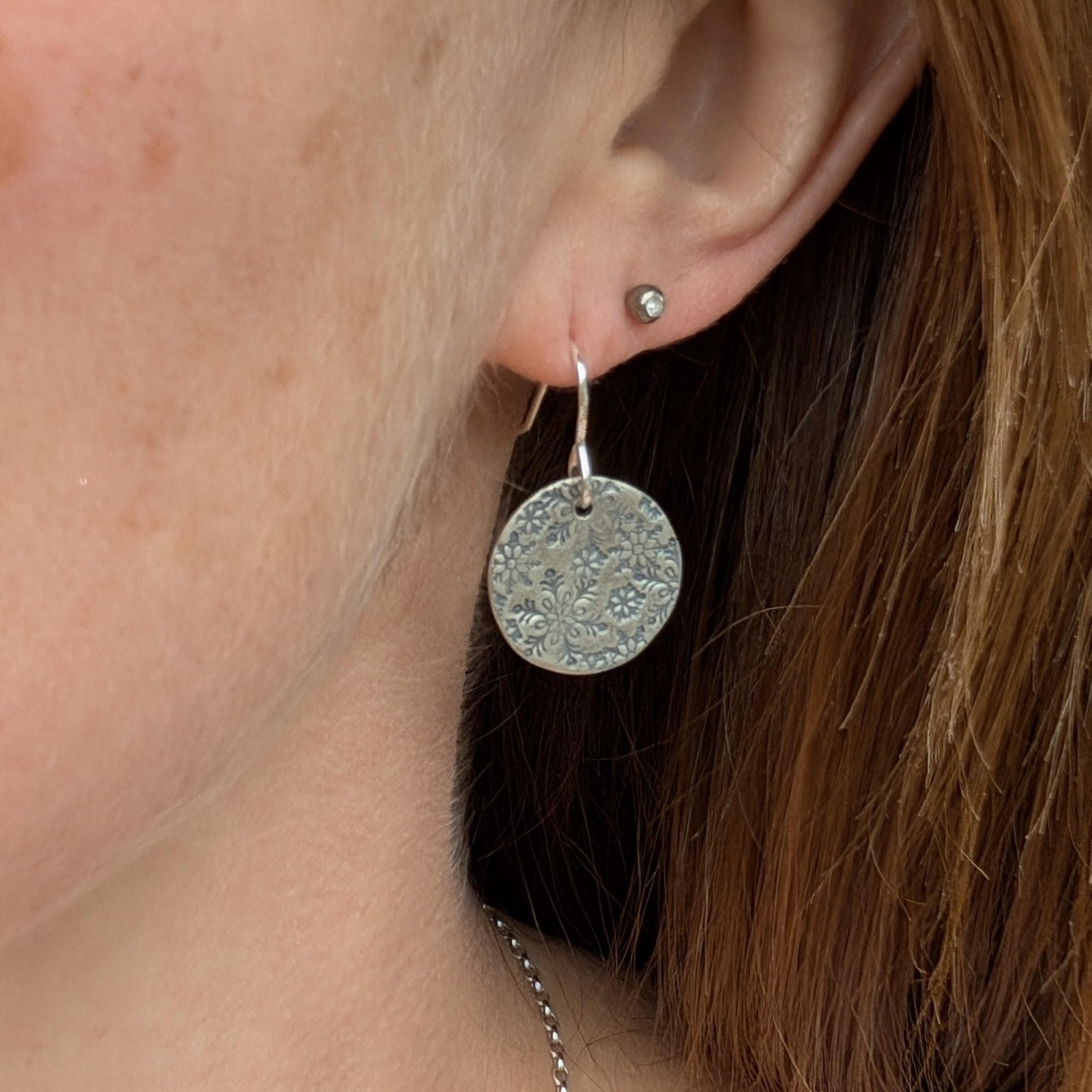 Silver snowflake disc earring worn on the ear, showcasing the delicate and detailed snowflake pattern, with a second stud earring visible in the upper piercing.