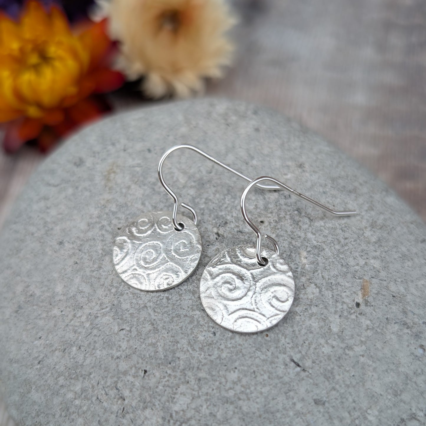 Silver Spiral Pattern Disc Earrings resting on a stone, showing hand cut discs with spiral pattern detail