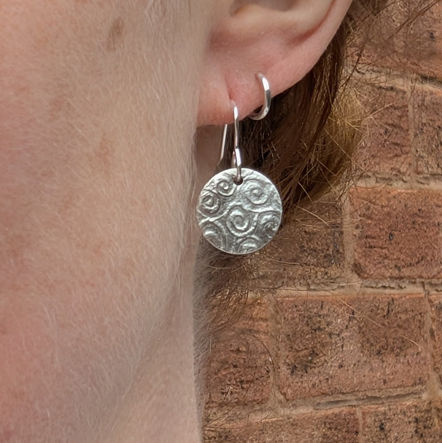 Silver Spiral Pattern Disc Earrings worn on ear, showing size and how the spiral pattern catches the light