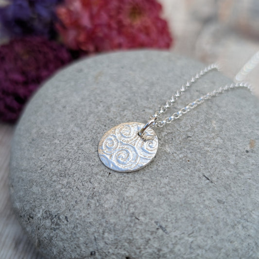 Silver Spiral Pattern Disc Necklace displayed on a stone with soft background and focus on the patterned silver disc