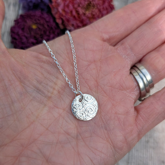 Silver Spiral Pattern Disc Necklace held in a hand to show size and detail of the spiral pattern