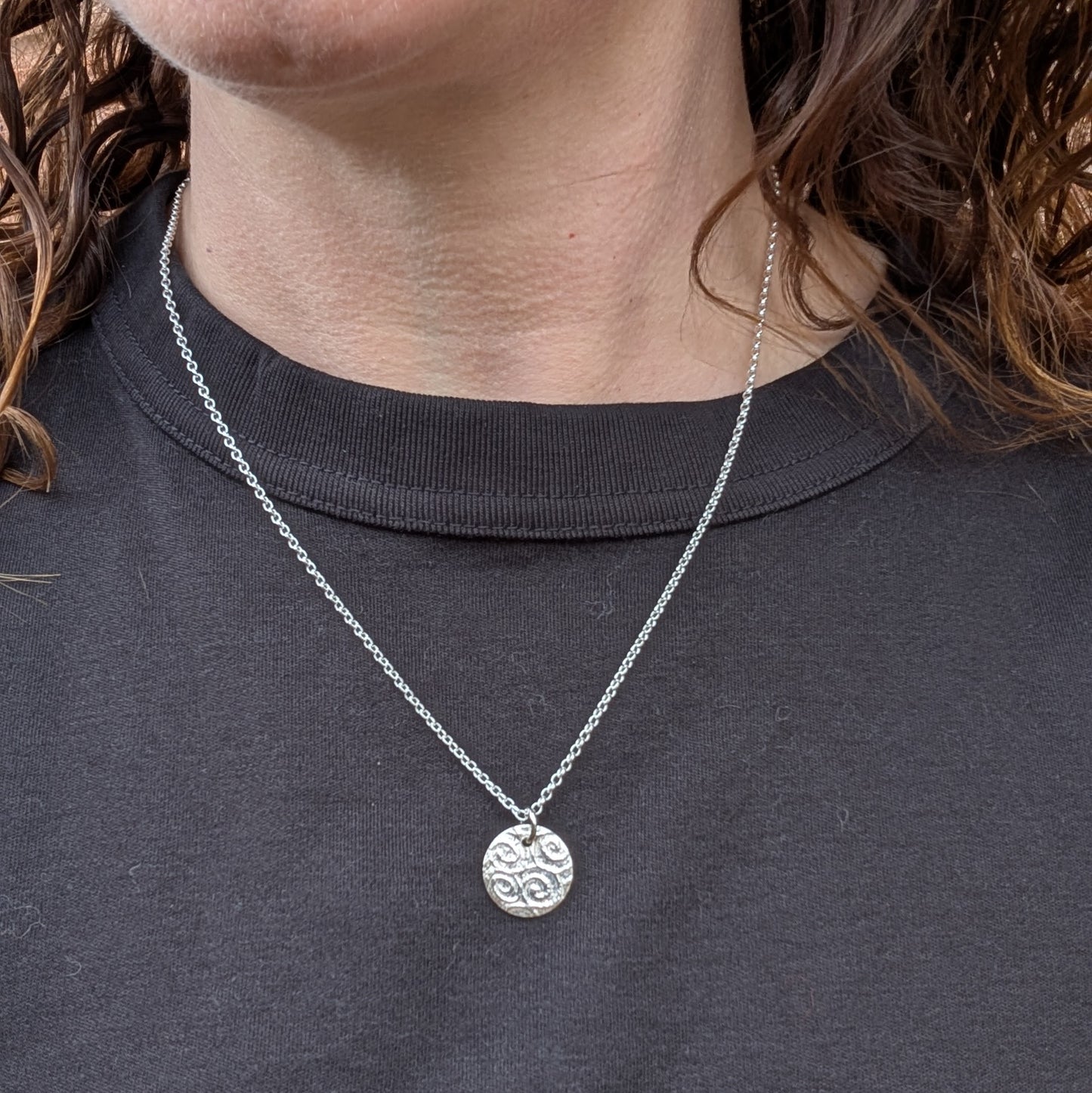 Silver Spiral Pattern Disc Necklace worn on a person with a dark top, showing how it sits on the neckline