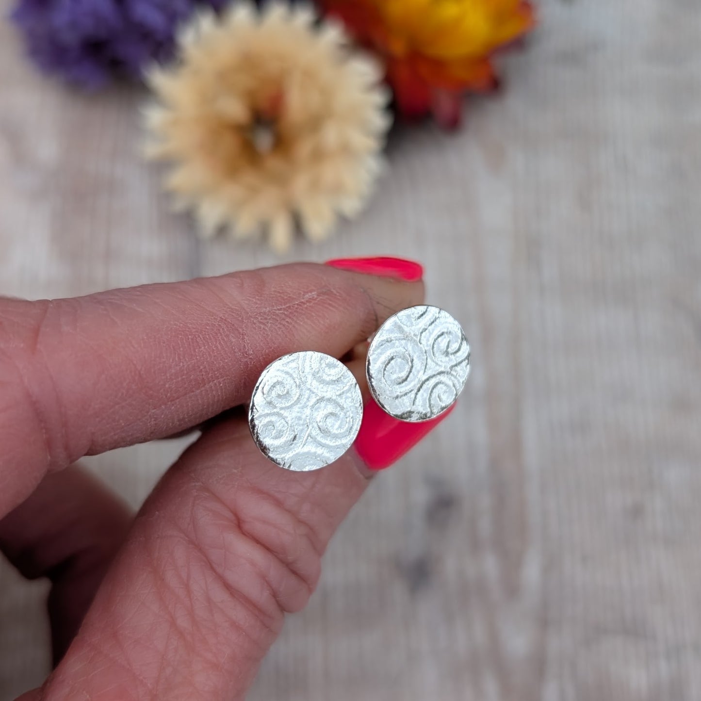 Silver Spiral Pattern Disc Stud Earrings held in hand, showing spiral pattern on round recycled sterling silver discs