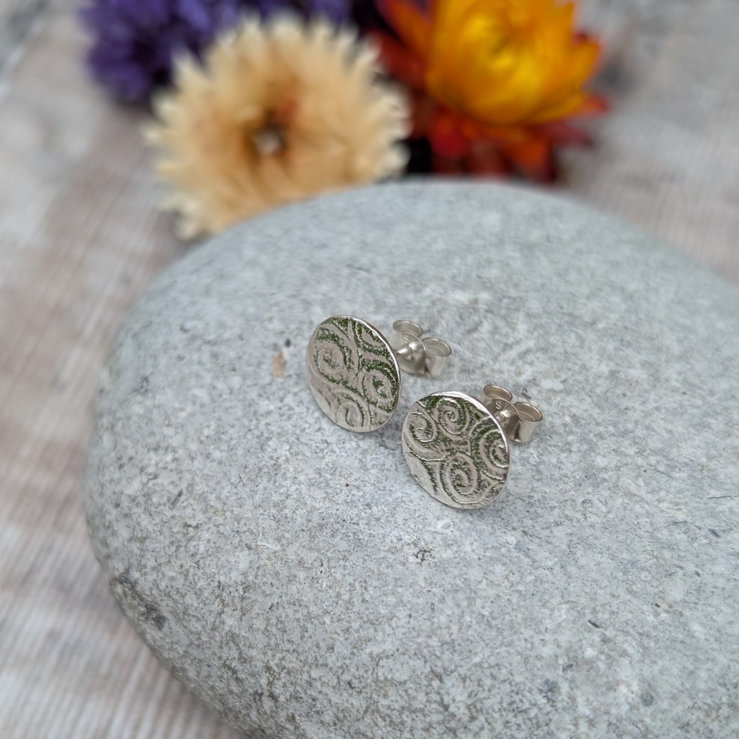 Silver Spiral Pattern Disc Stud Earrings on a stone from a slight angle, showing depth and pattern detail