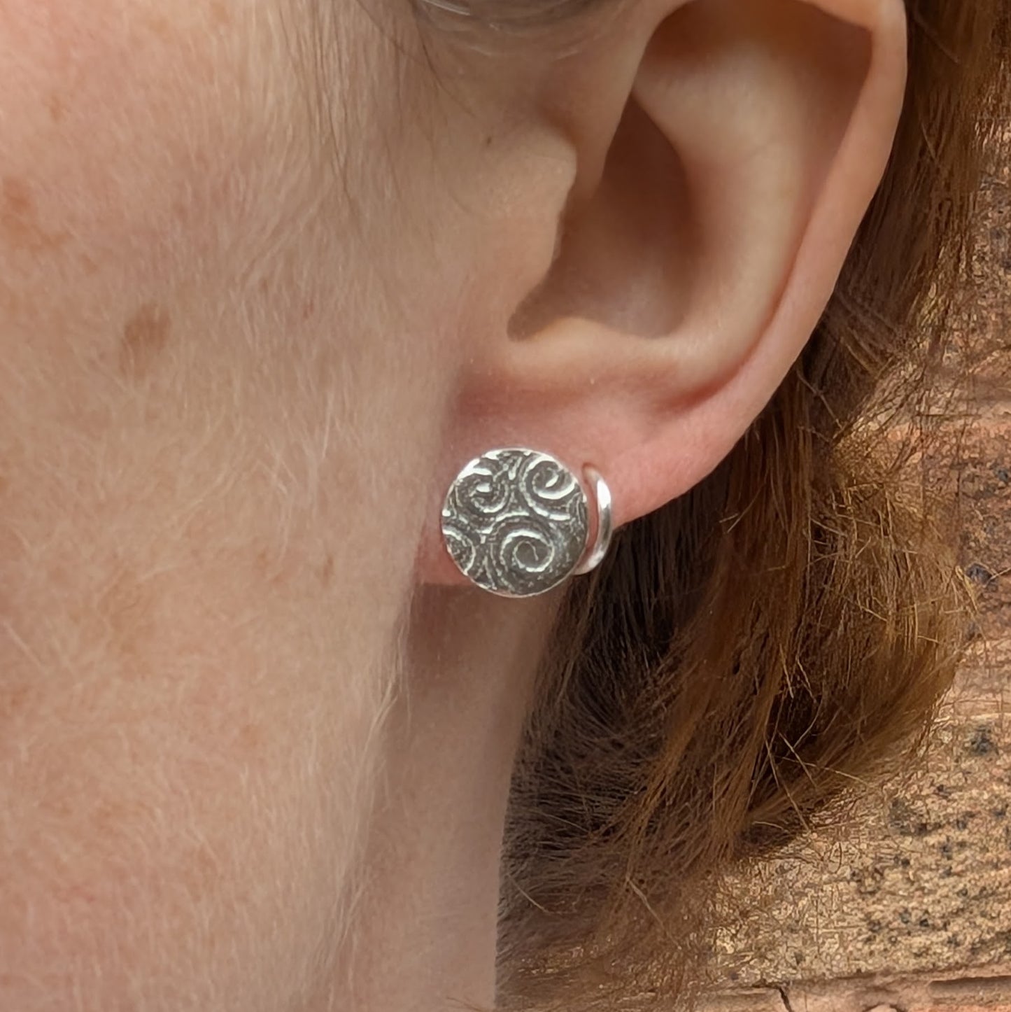 Silver Spiral Pattern Disc Stud Earrings worn on ear, showing size and how they sit when worn