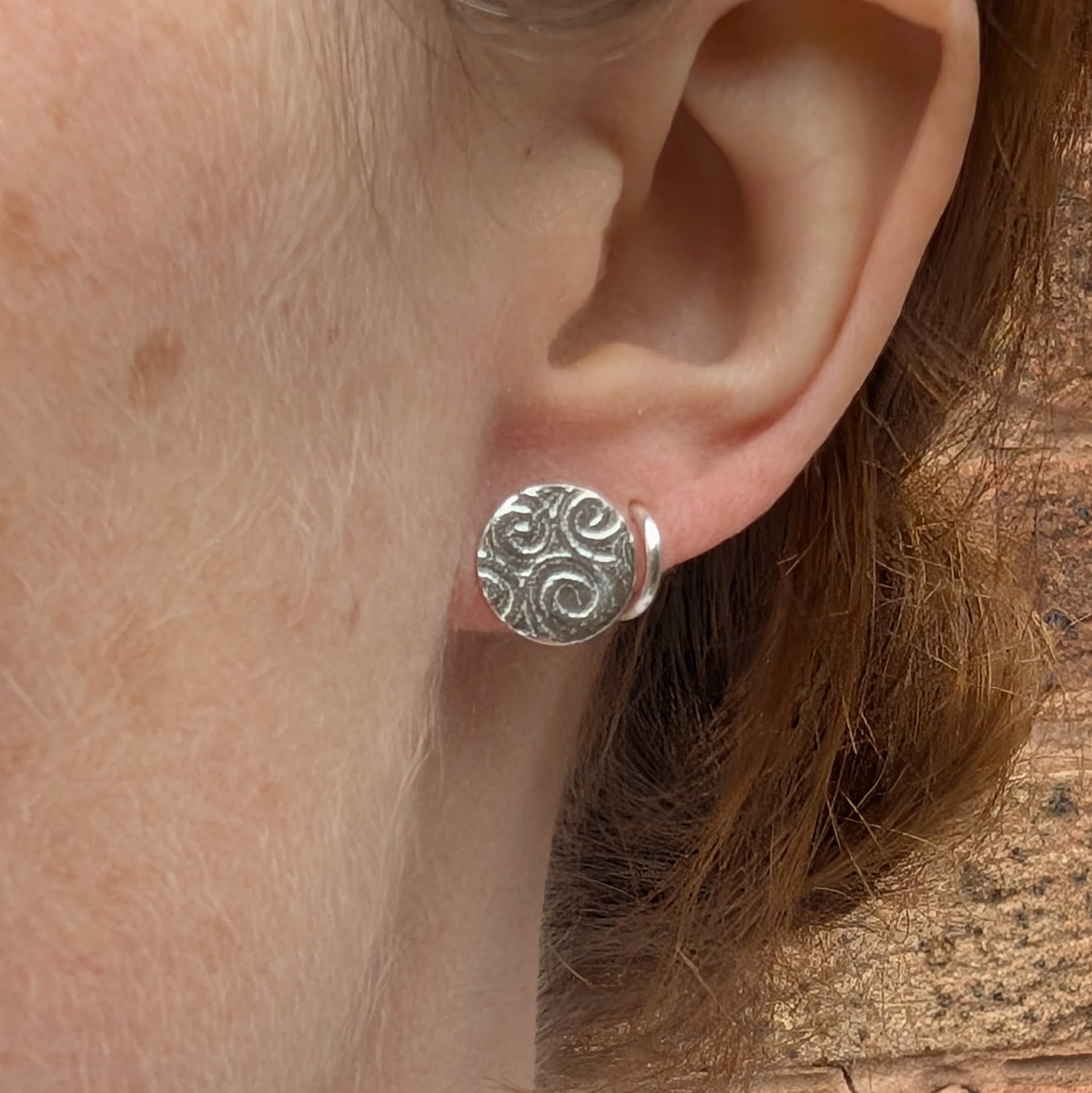 Silver Spiral Pattern Disc Stud Earrings worn on ear, showing size and how they sit when worn