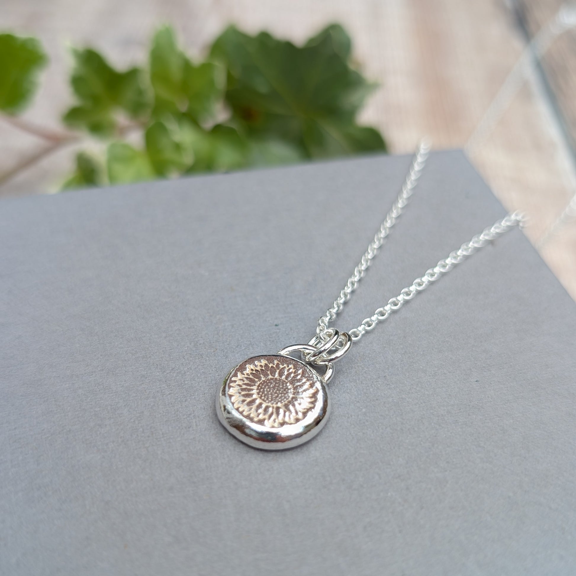 Silver Sunflower Pebble Necklace handmade from recycled Sterling Silver with a stamped sunflower design, displayed on a grey background.