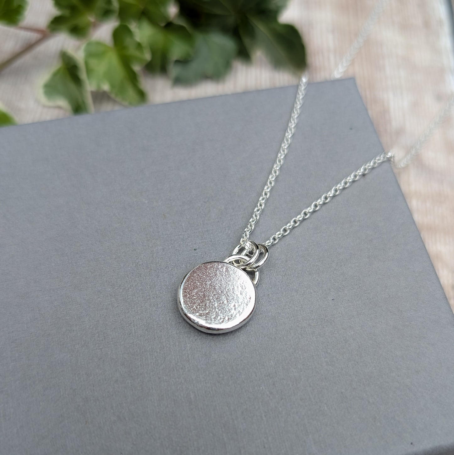 Back view of the handmade Silver Sunflower Pebble Necklace, showing the smooth recycled Sterling Silver pebble pendant and silver chain.