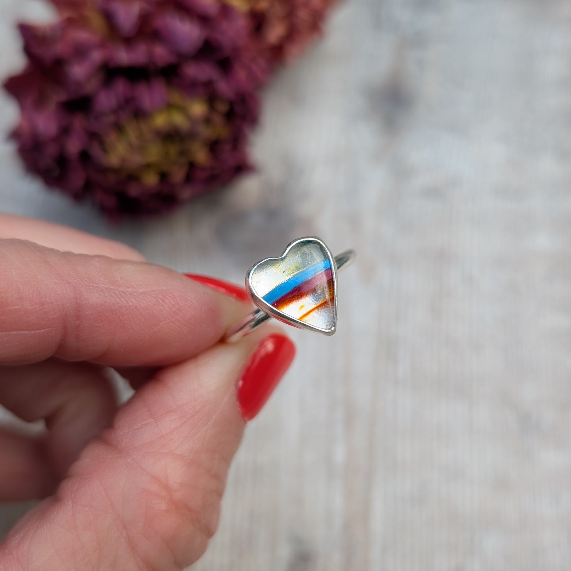 Close-up of the striped Surfite heart ring being held between fingers.
