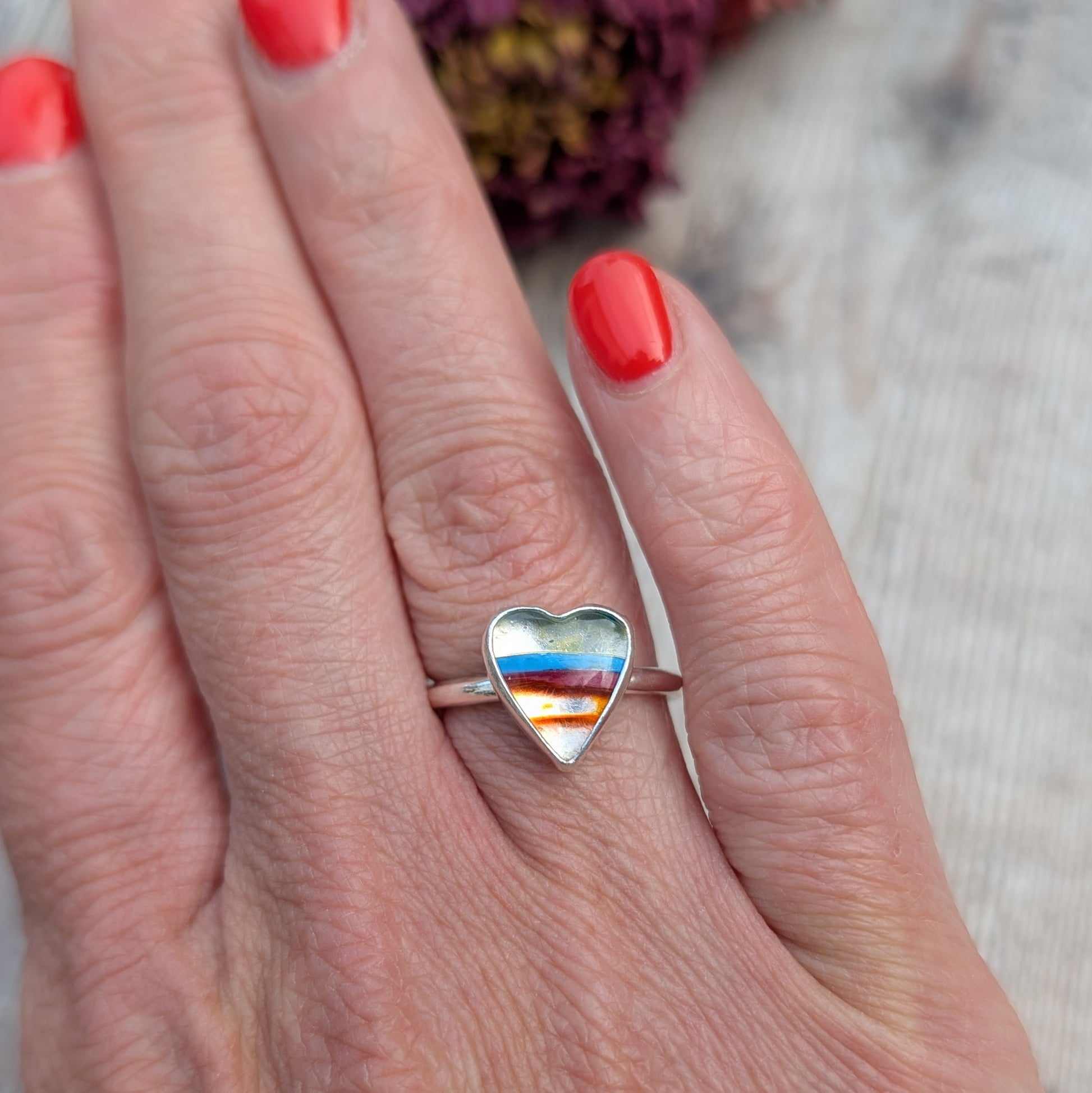Heart-shaped Surfite ring on hand, showing striped colours of red, blue, and orange in a silver setting.
