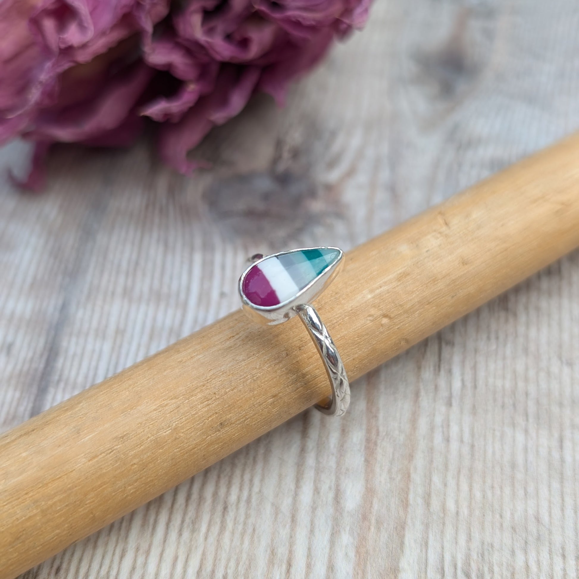 Handmade silver Surfite ring with a teardrop stone resting on a wooden ring mandrel, showing engraved band detail.