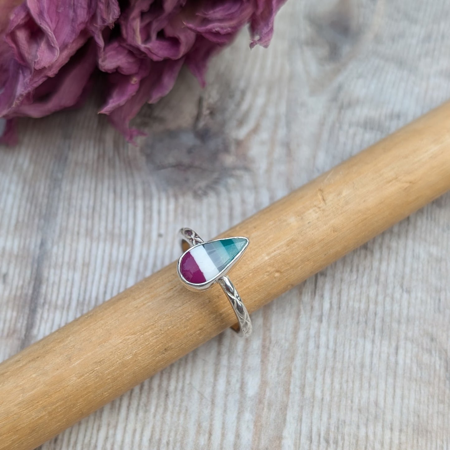 Handmade silver Surfite ring with a teardrop stone resting on a wooden ring mandrel, showing engraved band detail.